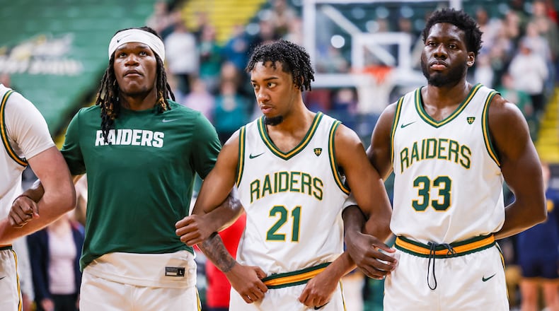Wright State junior guard Logan Woods (center) links arms with sophomore wing Andrea Holden (left) and graduate forward Michael Imariagbe (right) during the national anthem before an 86-37 win over Franklin College 86-37 in a season opener on Monday, Nov. 3 at Ervin J. Nutter Center in Fairborn. BRYANT BILLING/STAFF