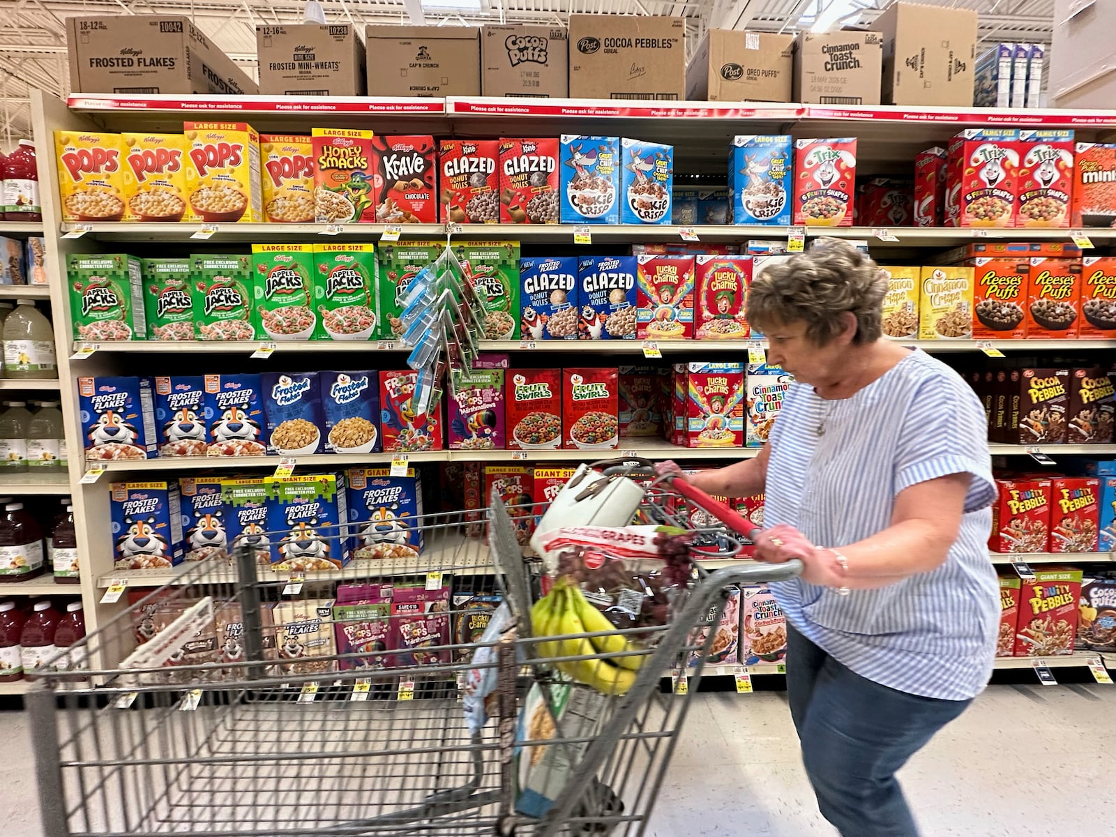 A woman pushes a shopping cart past boxes of Kellogg's breakfast cereal at a supermarket, Friday, July 11, 2025, in Springfield, Pa. (AP Photo/Matt Slocum)