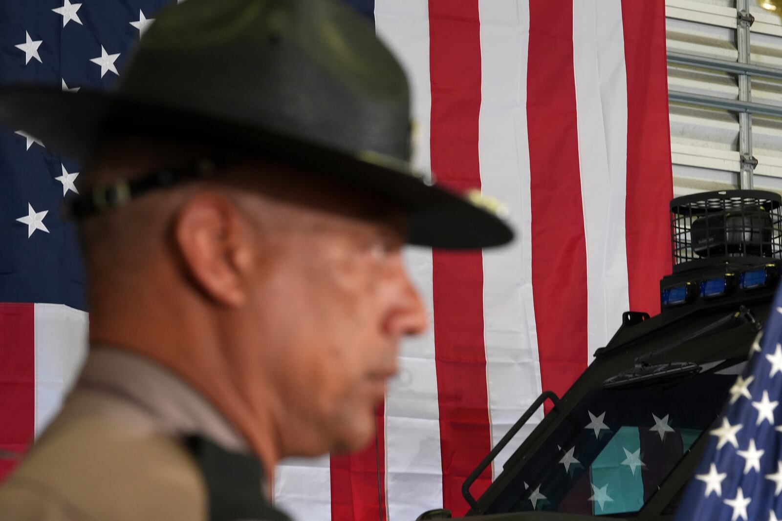 A member of the Florida Highway Patrol listens during a press conference on a recent immigration enforcement operation, with Gov. Ron DeSantis at the South Florida office of U.S. Immigration and Customs Enforcement and Enforcement and Removal Operations, Thursday, May 1, 2025, in Miramar, Fla. (AP Photo/Rebecca Blackwell)