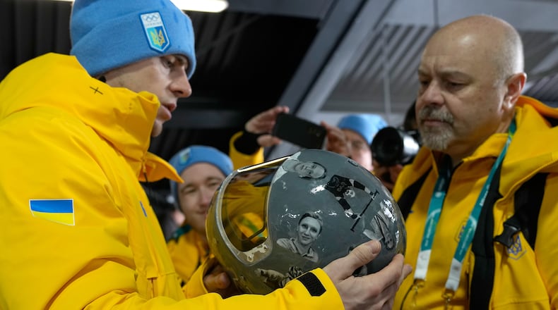 Ukrainian skeleton athlete Vladyslav Heraskevych left, holds his crash helmet at the mixed zone of the sliding center at the 2026 Winter Olympics, in Cortina d'Ampezzo, Italy, Thursday, Feb. 12, 2026. (AP Photo/Alessandra Tarantino)