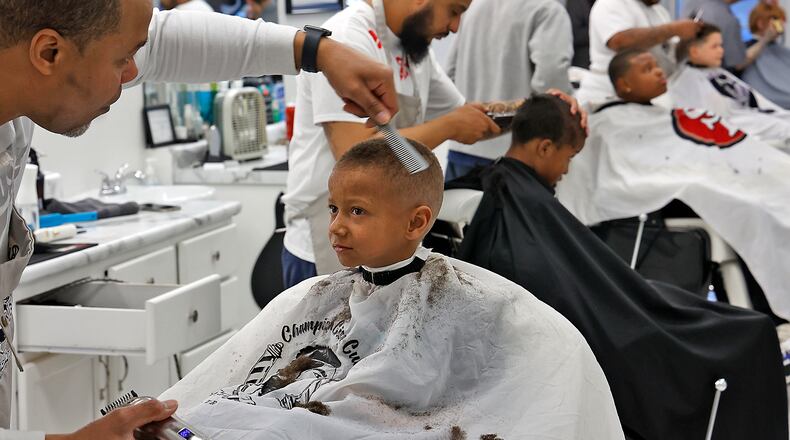 Maxx Johnson, 6, looks at Rufus Humphrey, one of the barbers at Champion City Cuts in the Southgate Shopping Center, as he cuts his hair Monday, March 6, 2023.. The five barbers volunteer their time the first Monday of every month to give Springfield City School students of all ages a fresh cut and some pizza as they wait their turn in the chair. The haircuts are offered as an incentive by the school district each month for good attendance. BILL LACKEY/STAFF