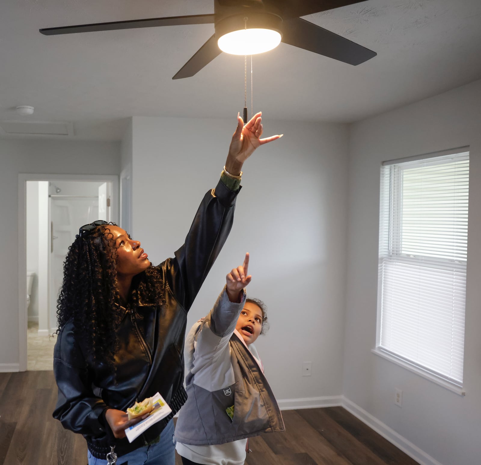 Imani Fudge, left, and her cousin Rileyanna Foster, 8, collaborate to turn on the lights following a home dedication hosted by the Habitat for Humanity of Greater Dayton on Friday, Dec. 12, 2025, in Springfield. The ceremony was for Foster and her grandmother Gwendolyn Iheme, who will live in this house. JOSEPH COOKE/STAFF