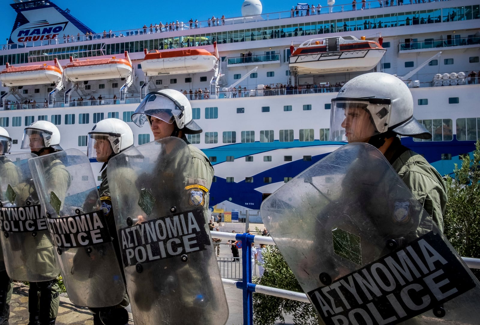 Riot police stand guard during the arrival of a ship carrying Israeli tourists, background, in Agios Nikolaos port, on the island of Crete, Greece, Tuesday, July 29, 2025. (Antonis Zouridakis/Eurokinissi via AP)