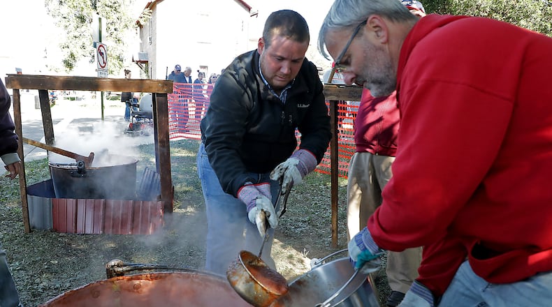 Jacob Manning, left, and Craig Justice scoop out apple butter from a kettle once it was finished cooking Saturday at the Enon Apple Butter Festival. The festival, which features food and crafts for sale, runs through Sunday. BILL LACKEY/STAFF