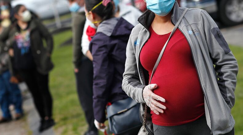 FILE - In this Thursday, May 7, 2020 file photo, a pregnant woman wearing a face mask and gloves holds her belly as she waits in line for groceries with hundreds during a food pantry sponsored by Healthy Waltham for those in need due to the COVID-19 virus outbreak, at St. Mary's Church in Waltham, Mass. One of the largest reports on Moderna or Pfizer COVID-19 vaccination in pregnancy bolsters evidence that it is safe although more rigorous research is needed. The new evidence from researchers at the Centers for Disease Control and Prevention was published Wednesday, April 21, 2021, in the New England Journal of Medicine. Johnson & Johnson’s now paused vaccine was not included. (AP Photo/Charles Krupa)