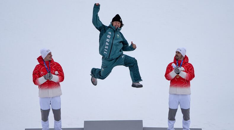 Brazil's Lucas Pinheiro Braathen, center, winner of an alpine ski, men's giant slalom race, jumps in celebration on the podium flanked by second placed Switzerland's Marco Odermatt, left, and third placed Switzerland's Loic Meillard, at the 2026 Winter Olympics, in Bormio, Italy, Saturday, Feb. 14, 2026. (AP Photo/John Locher)