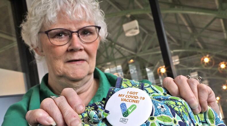 Linda Gast shows the COVID-19 vaccine button she wears on her backpack Tuesday, August 30, 2022. Since contracting COVID and dealing with it's effects for the past two years, she encourages everyone to get vaccinated. BILL LACKEY/STAFF