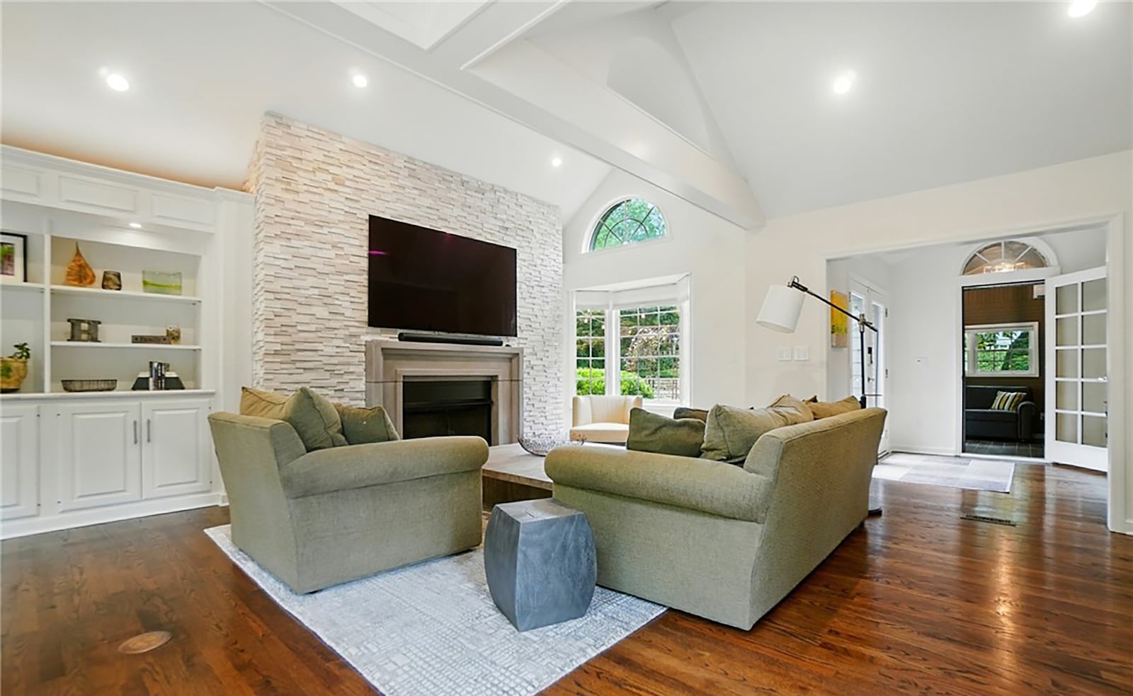 The great room has a stacked stone floor to ceiling fireplace, vaulted ceilings and recessed lighting and a built in bookcase with cabinets.