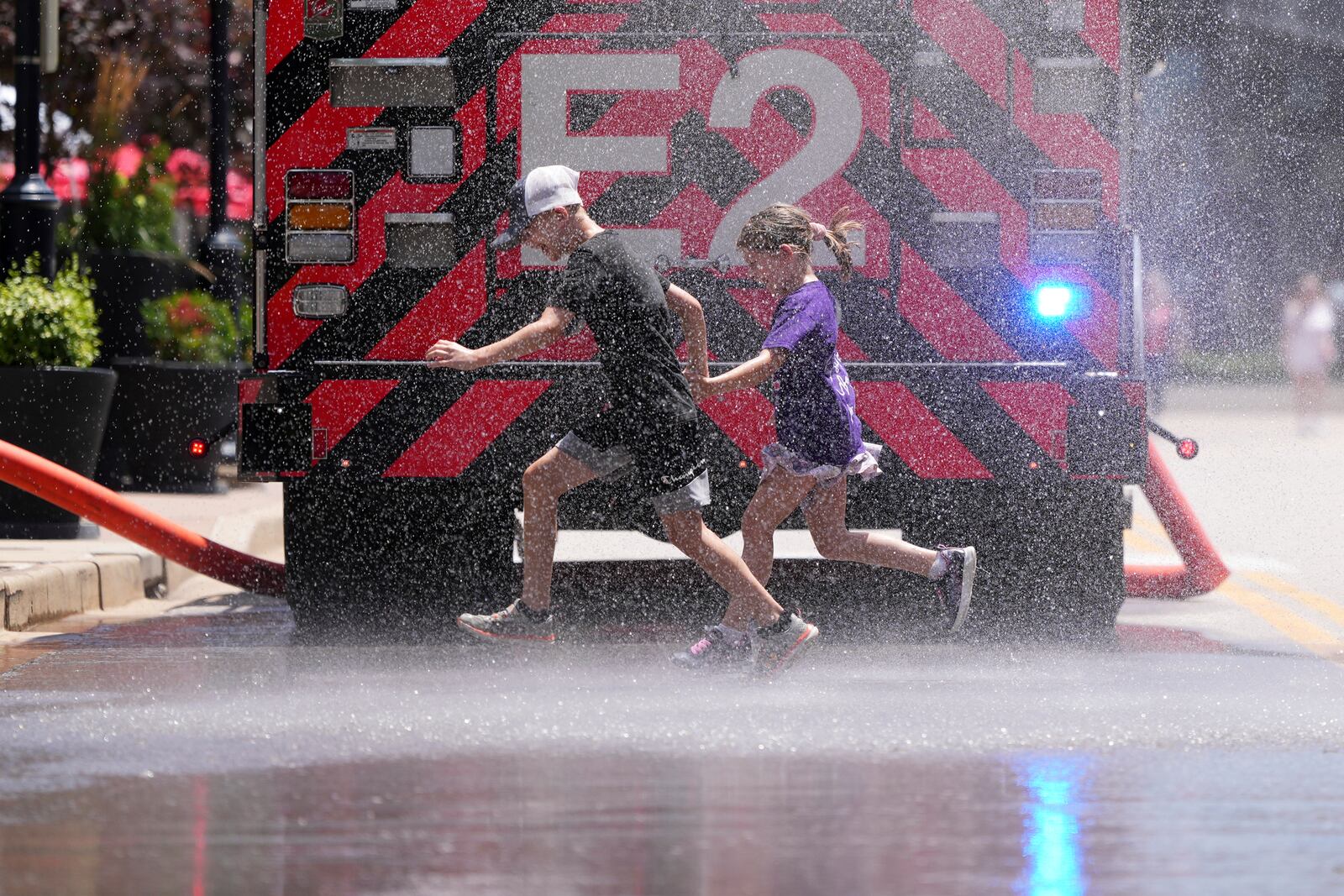 Children run through water sprayed by a fire truck to cool off outside Busch Stadium before the start of a baseball game between the St. Louis Cardinals and the Cincinnati Reds Sunday, June 22, 2025, in St. Louis. (AP Photo/Jeff Roberson)