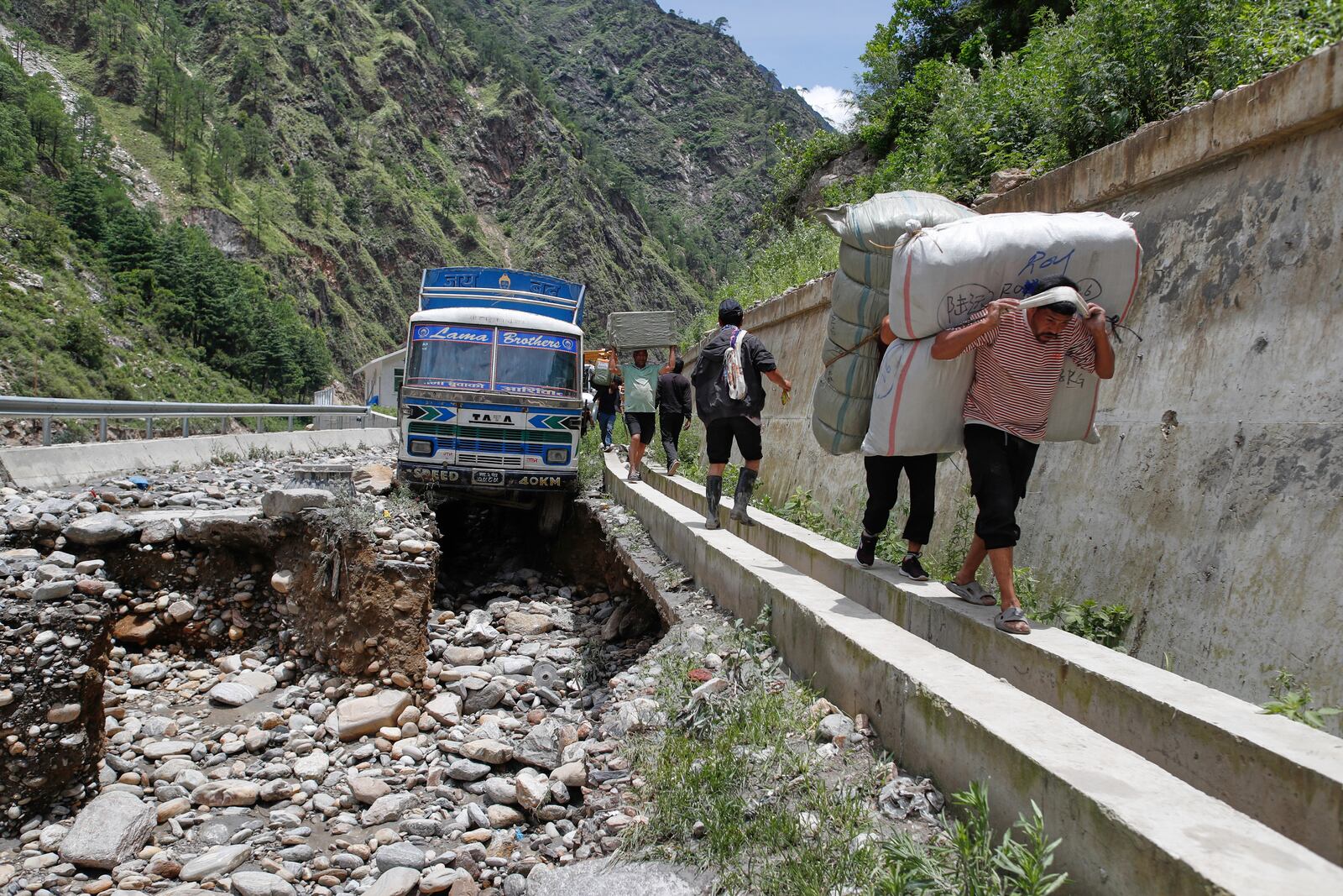 Porters carry goods from a damaged truck stuck after monsoon rains swept away a key bridge connecting the country with China at Rasuwagadi, 120 kilometers (75 miles) north of the capital, Kathmandu, Nepal, Wednesday, July, 9, 2025. (AP Photo/Sujan Gurung)