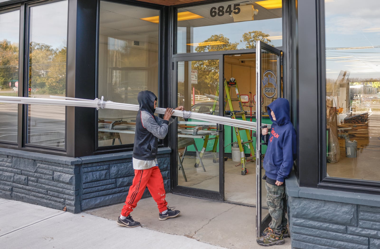 Marvin Rodriguez prepares to do construction in the upcoming Nifty Thrifties Bargain Bins as Cameron Penwell, 12, holds the door on Friday, October 31, 2025, in Enon. The store is planned to open in November. JOSEPH COOKE/STAFF