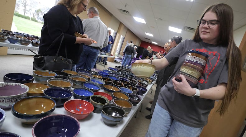 Liv Hamilton, a volunteer at the annual Empty Bowls fundraiser at Wittenberg University's student center, places more of the unique, handmade bowls out on a table so patrons can choose the one they want Thursday, March 27, 2025. The Wittenberg Department of Art holds the fundraiser annually to raise money for Second Harvest Food Bank. Community members purchase the bowl they want and get to enjoy some soup in the student center dining hall. Several hundred people attended the event. BILL LACKEY/STAFF