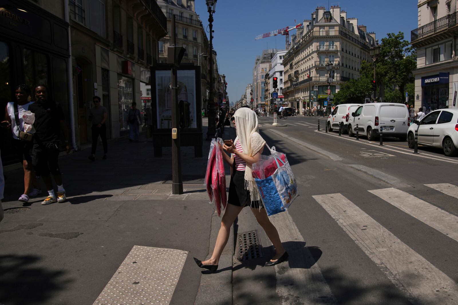 A woman protects her head during a heat wave, Monday, June 30, 2025 in Paris. (AP Photo/Christophe Ena)