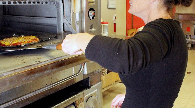 Enon Pizza and Company owner Tracy Wiggins checks to see if a pizza is done cooking. JEFF GUERINI/STAFF