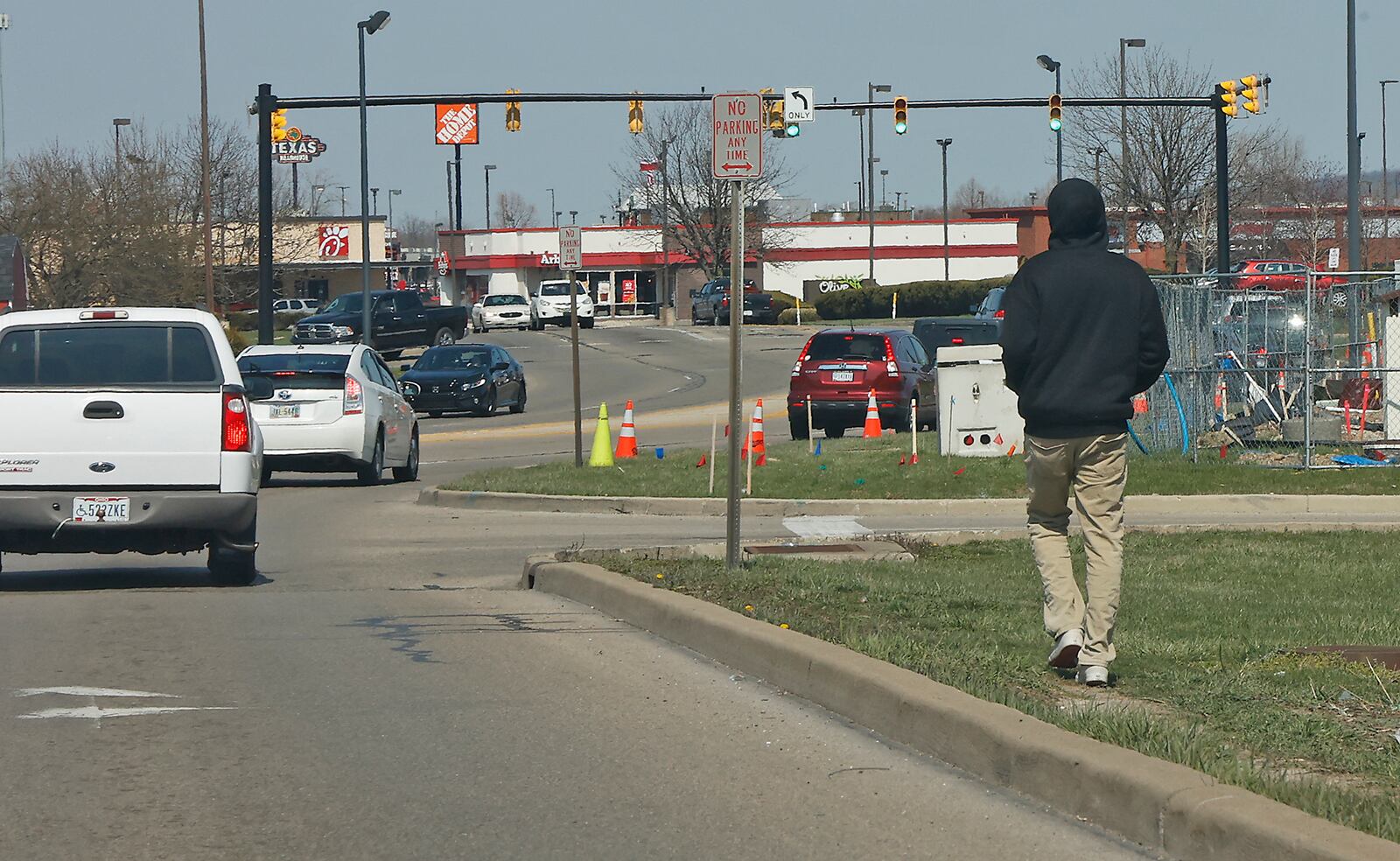 A man walks in the grass along Bechtle Avenue Thursday, March 30, 2023. The City of Springfield plans to install sidewalks along the busy roadway. BILL LACKEY/STAFF