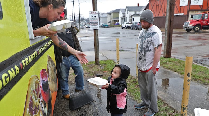 Rae’lyn Moore, 4, gets a free meal from Kim Poole, owner of Freddie’s Franks & Burgers food truck, Wednesday. Due to the coronavirus, the Springfield Soup Kitchen is not allowed to open, so they got Kim and her husband, Fred, to park their food truck in the parking lot across the street from the soup kitchen and are feeding people outdoors. BILL LACKEY/STAFF
