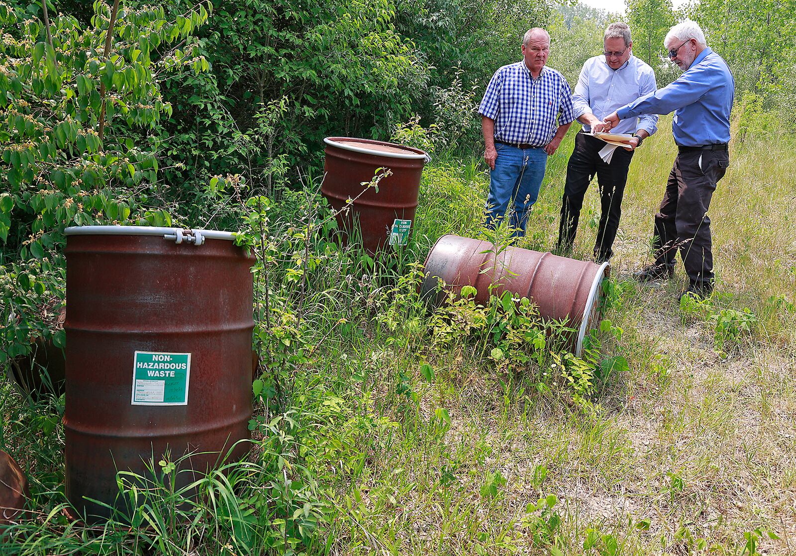 Bob Rule, from the RESA II "responsible party" group, center, along with German Township Trustee Rodney Kaffenbarger, left, and Larry Ricketts of People for Safe Water, look over a map for the Tremont City Barrel Fill on Wednesday, June 7, 2023. The barrels at left were empty but 1.5 million gallons of hazardous waste was buried in the ground at the site. BILL LACKEY/STAFF