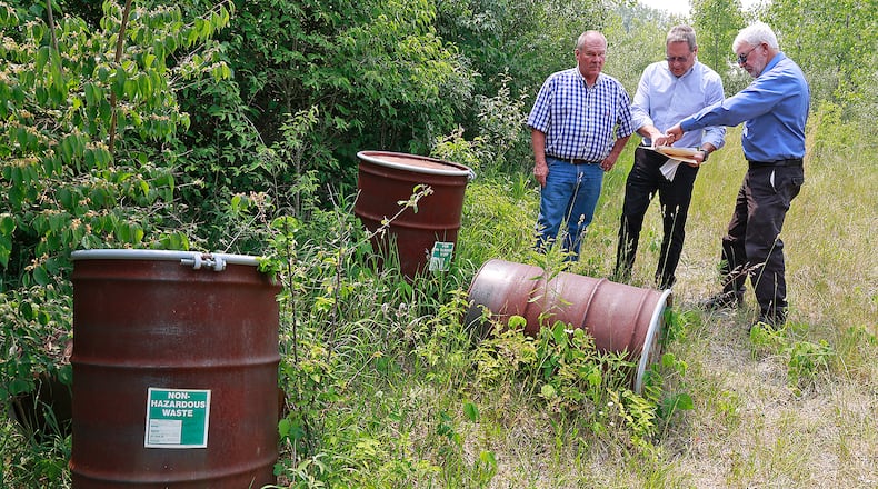 Bob Rule, from the RESA II "responsible party" group, center, along with German Township Trustee Rodney Kaffenbarger, left, and Larry Ricketts of People for Safe Water, look over a map for the Tremont City Barrel Fill on Wednesday, June 7, 2023. The barrels at left were empty but 1.5 million gallons of hazardous waste was buried in the ground at the site. BILL LACKEY/STAFF