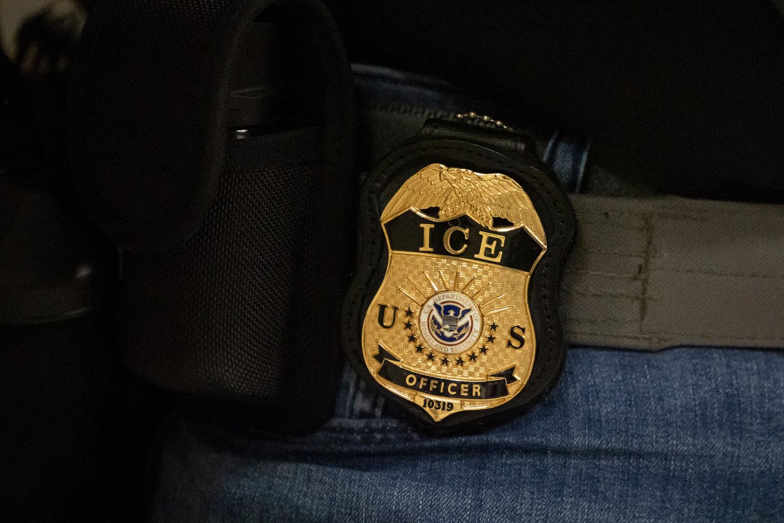 A federal agent wears a badge of Immigration and Customs Enforcement while standing outside an immigration courtroom at the Jacob K. Javits Federal Building in New York, Tuesday, June 10, 2025. (AP Photo/Yuki Iwamura)
