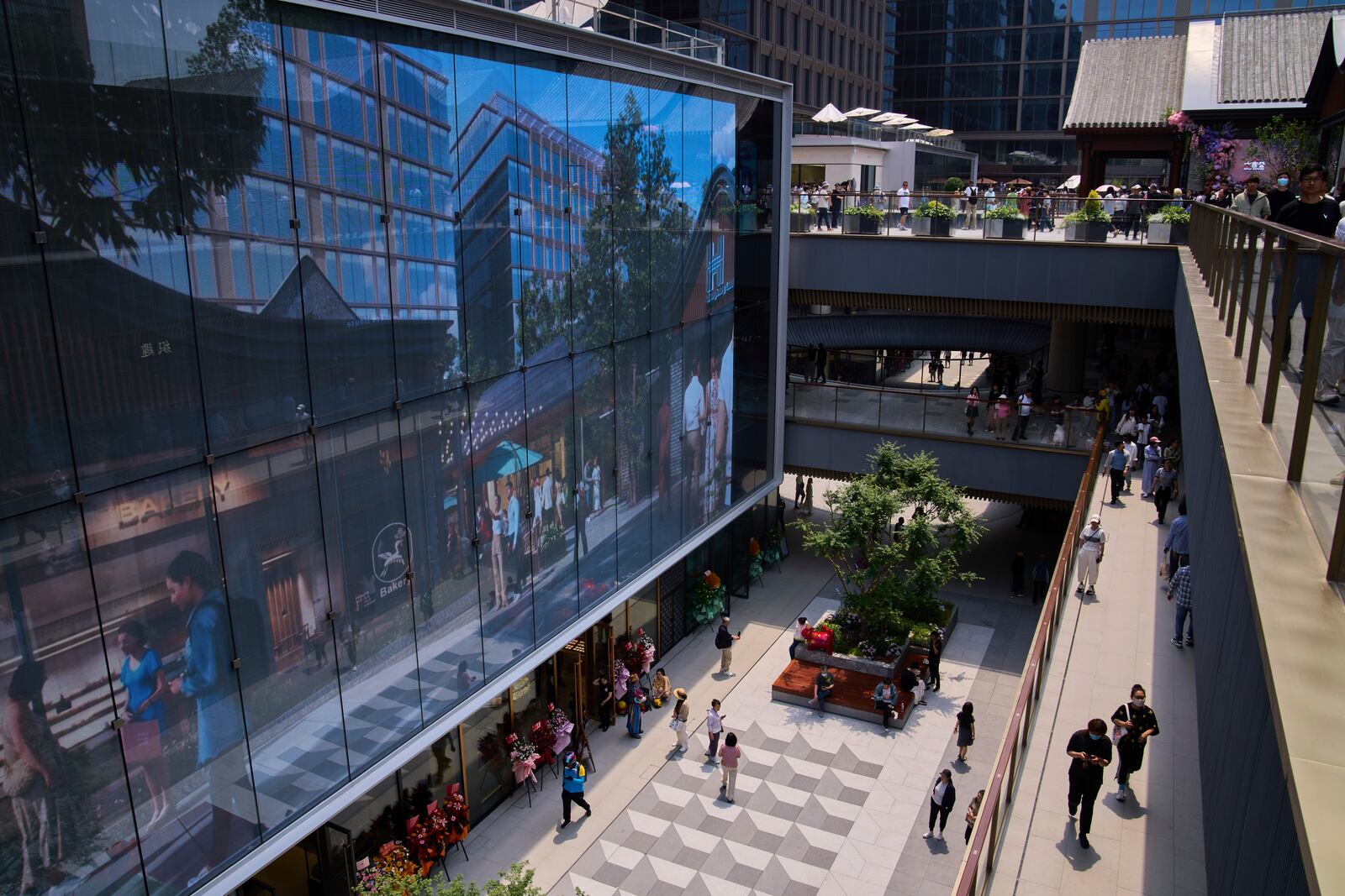 People tour by a projector screen promoting a newly opened outdoor Hutong style shopping mall, in Beijing, Monday, May 26, 2025. (AP Photo/Andy Wong)