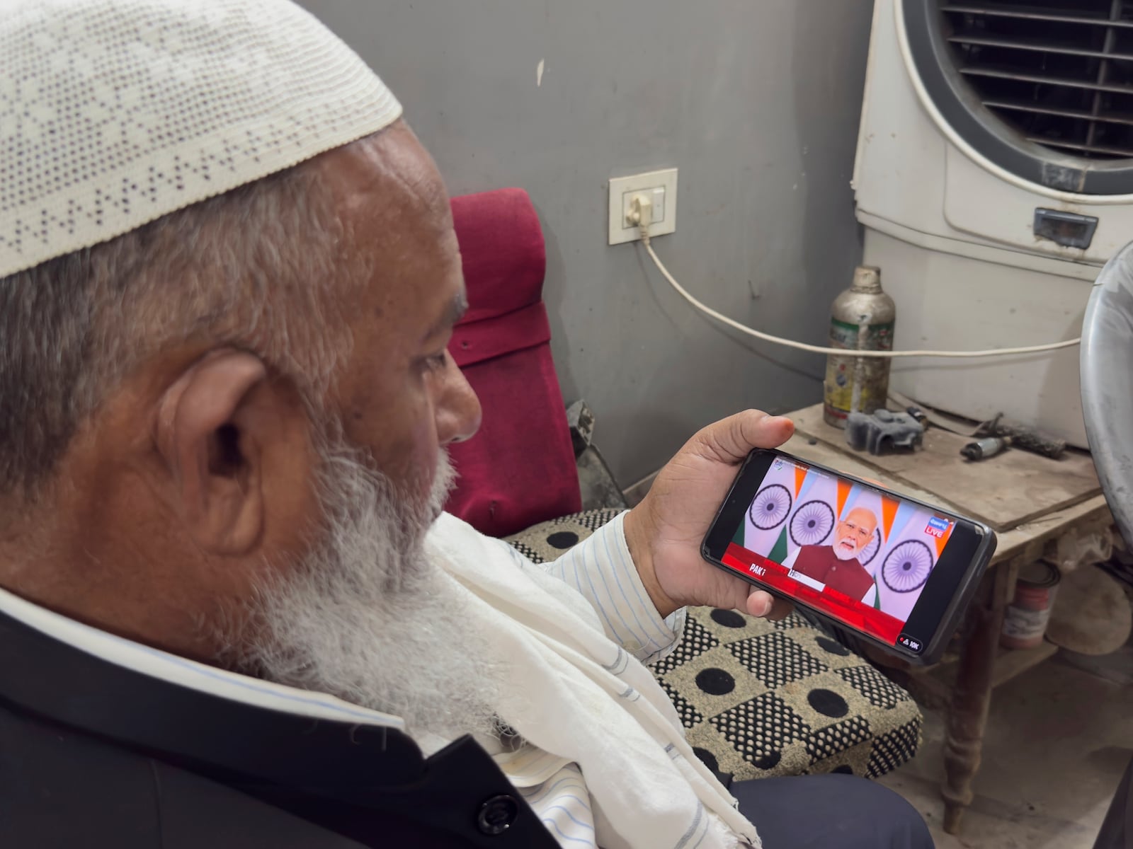 An Indian muslim shopkeeper watches on a phone the live telecast of Indian Prime Minister Narendra Modi's speech on television screens, in Prayagraj, in the northern Indian state of Uttar Pradesh, India, Monday, May 12, 2025. (AP Photo/Rajesh Kumar Singh)