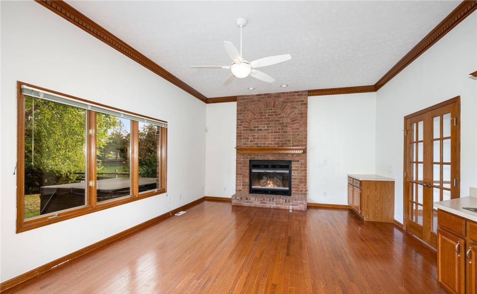 The family room has hardwood floors, a ceiling fan, crown molding, French doors and a wet bar. There is a brick gas fireplace at one end. CONTRIBUTED