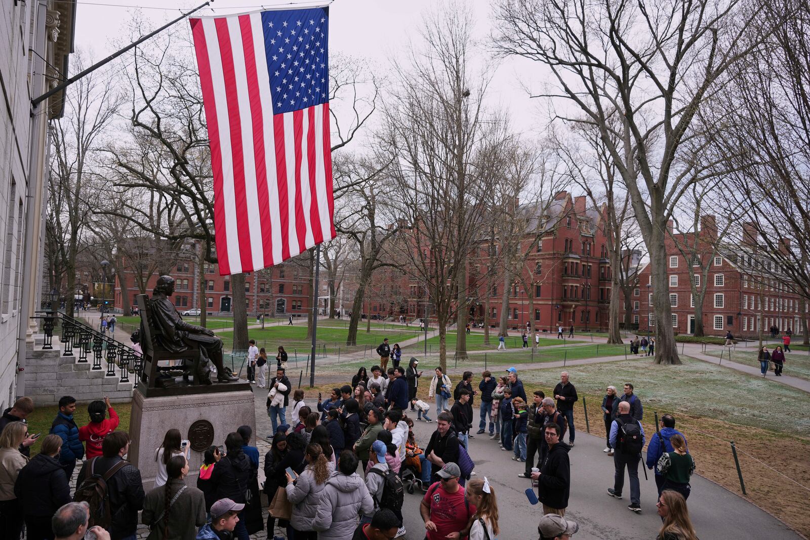Visitors stop at the statue of John Harvard in Harvard Yard at Harvard University, Tuesday, April 15, 2025, in Cambridge, Mass. (AP Photo/Charles Krupa)