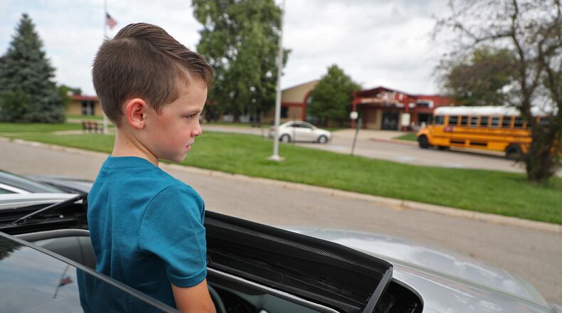 Ty Siri keeps an eye out for his big sister as he stands through the sunroof of his mother's car while waiting for school to release early at Indian Valley School in Enon on Aug. 26. The Greenon school district was one of several schools that released early because of the heat. BILL LACKEY/STAFF