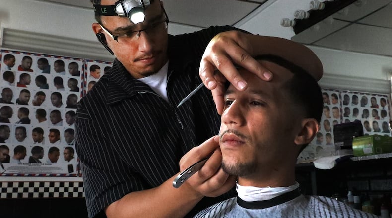 Alex Robinson, owner of Robinson Corner Cutz, uses a camping headlamp to cut Wesley Patterson hair Friday when the power went out during a thunderstorm. Patterson said he has appointments scheduled all day so when the power went out he went home and got the headlamps and a generator to power his clippers. BILL LACKEY/STAFF