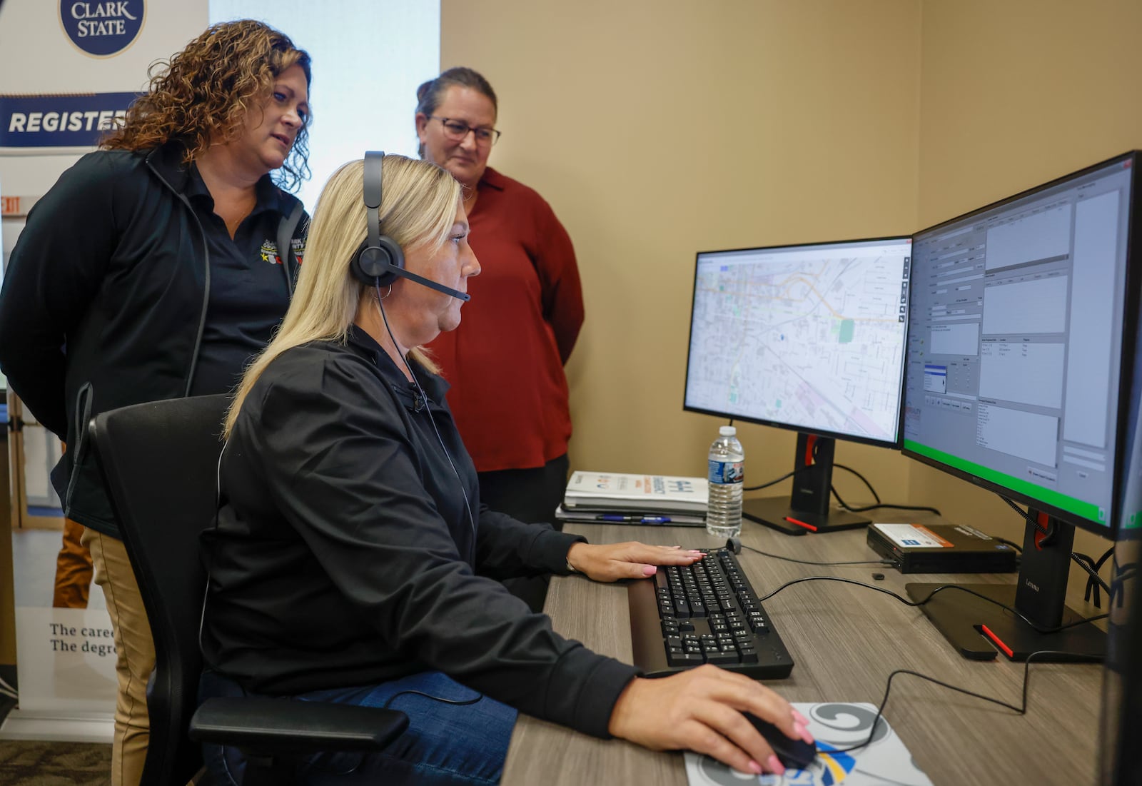 Tracy Yates, seated, director of outreach and recruitment for the Clark County Sheriff's Office, works on a computer as Alisha Lemen, left, operations manager for Clark County Communications 911 Center, and Mindy Lane, 911 dispatch instructor for Clark State, supervise in the 911 communications dispatch room on Friday at Clark State's Xenia campus. Clark State College opened its 911 Dispatch Academy in September 2025 to address staffing shortages in emergency communication centers. JOSEPH COOKE / STAFF