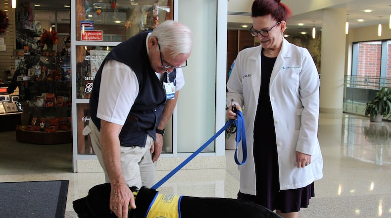 Larry Miller, a volunteer for Mercy Health Springfield Regional Medical Center, pets service dog in training Burbank as he accompanies his handler Dr. Lynne Eaton during her daily rounds. HASAN KARIM/STAFF