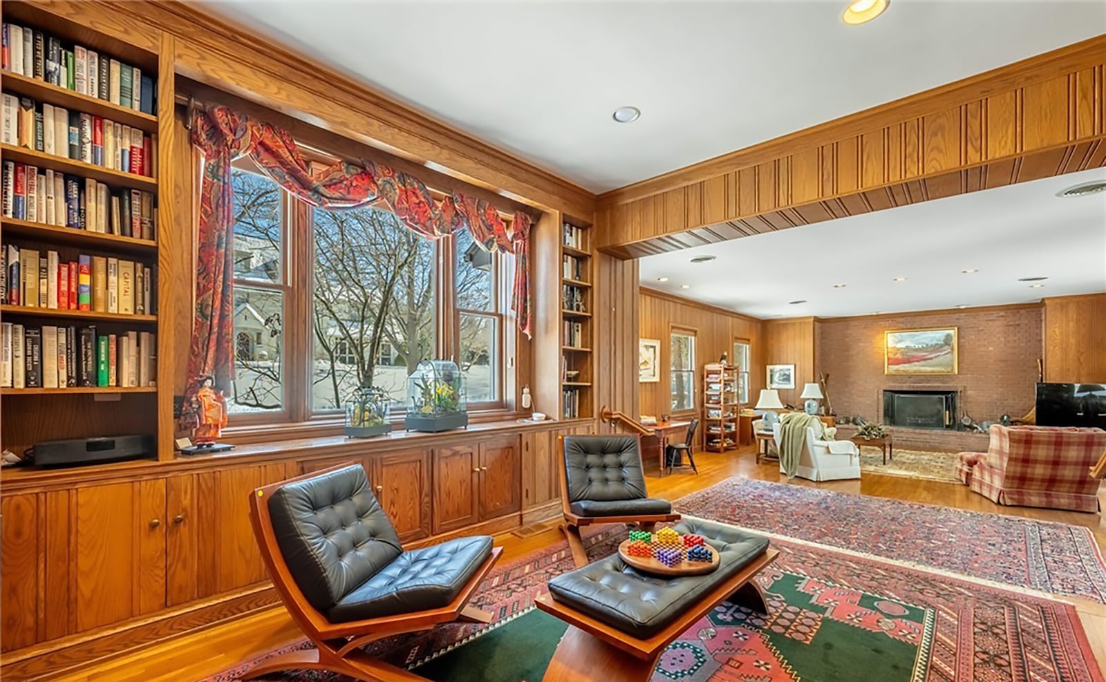 The study has wood paneled walls and built in bookcases with cabinets. Hardwood floors continue two steps down into the family room, which features a brick woodburning fireplace and two additional built in bookcases. CONTRIBUTED