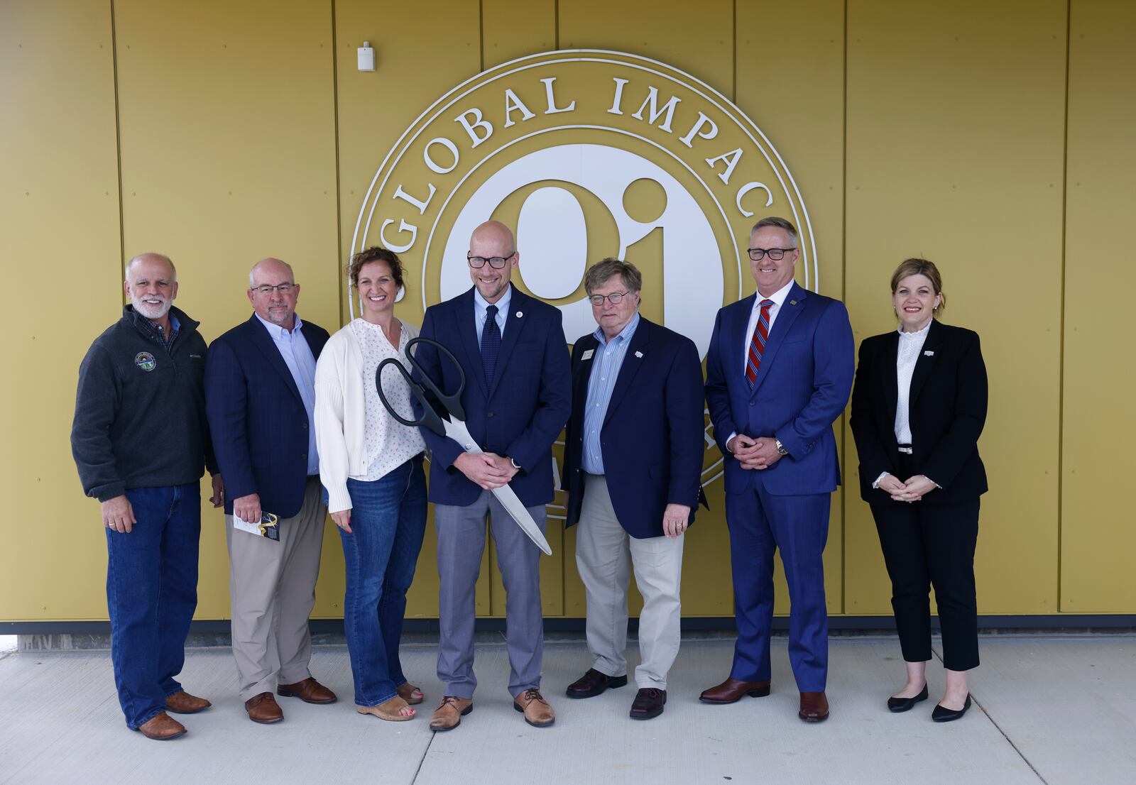 Josh Jennings, center, founding director of Global Impact STEM Academy, takes a photo with a group after cutting the ribbon during a ceremony to celebrate the new upper academy of the Global Impact STEM Academy on Friday, May  23, 2025, at Clark State College. JOSEPH COOKE/STAFF