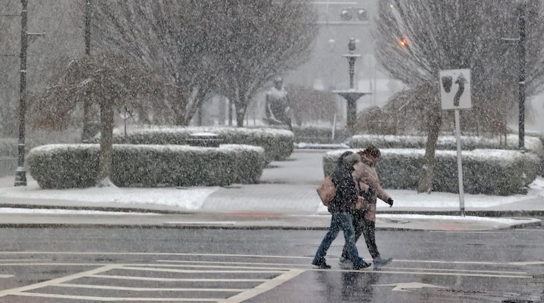 The snow Friday, Feb. 16, 2024 partially obscures two people as they cross Fountain Avenue in downtown Springfield. BILL LACKEY/STAFF