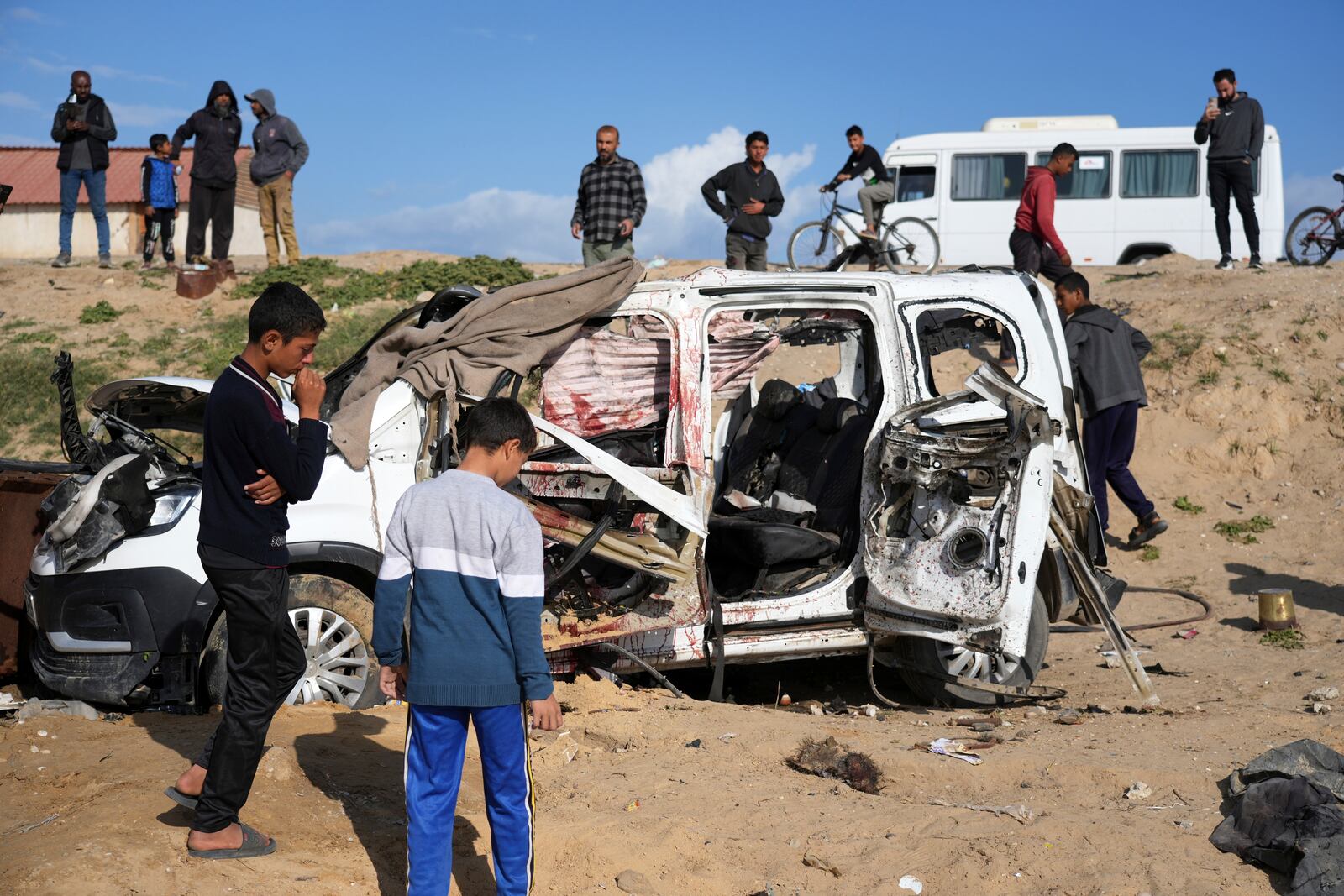 Palestinians look at the wreckage of a car struck earlier by an Israeli army attack that killed at least seven people, six of them the Abu Mahadi brothers, in the outskirts of Deir al-Balah, central Gaza Strip, Sunday, April 13, 2025. (AP Photo/Abdel Kareem Hana)