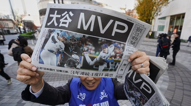 Staff of Japan's newspaper The Asahi Shimbun holds aloft a copy of the extra issue published after the Los Angeles Dodgers Shohei Ohtani won a Most Valuable Player award, in Tokyo, Friday, Nov. 14, 2025. (AP Photo/Koji Ueda)