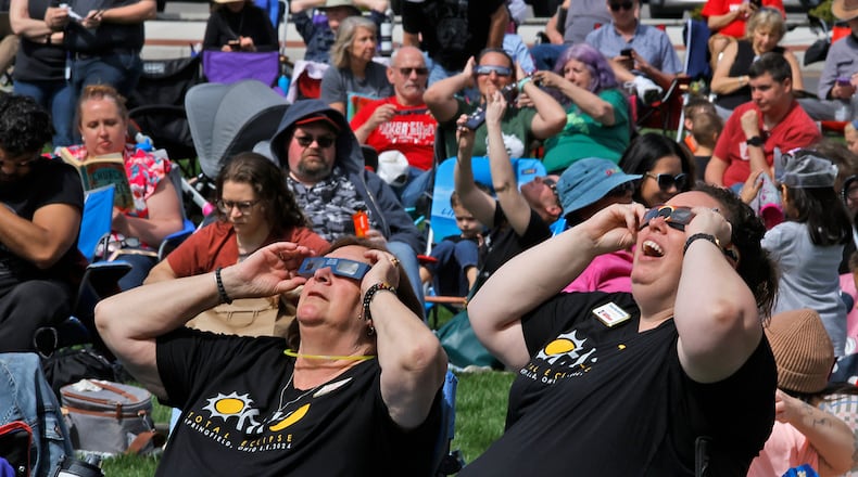 Michelle Hemphill, left, and Teresa Blue-McWhorter watch the solar eclipse start to form over National Road Commons Park Monday, April 8, 2024. BILL LACKEY/STAFF
