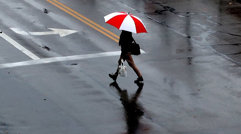 A man and his umbrella are reflected in wet pavement as he crosses Bechtle Avenue in the rain. BILL LACKEY/STAFF