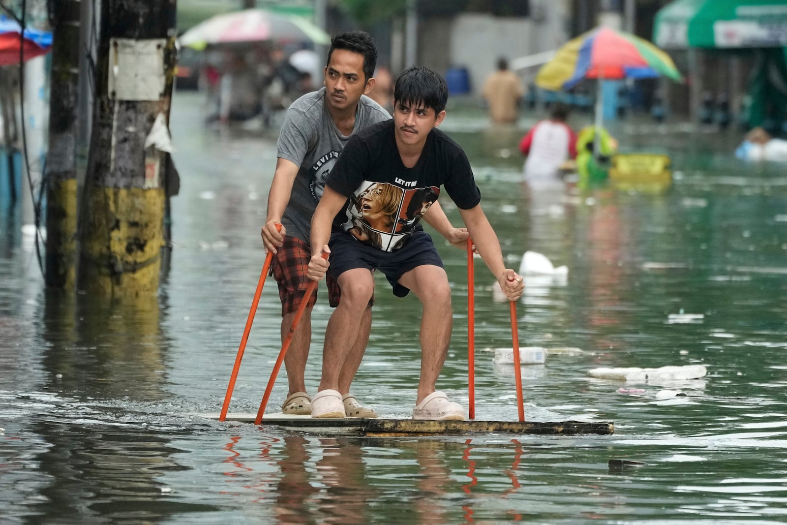 Residents use poles as they ride an improvised float along a flooded road as Typhoon Co-may intensified seasonal monsoon rains at Malabon city, Philippines on Friday, July 25, 2025. (AP Photo/Aaron Favila)