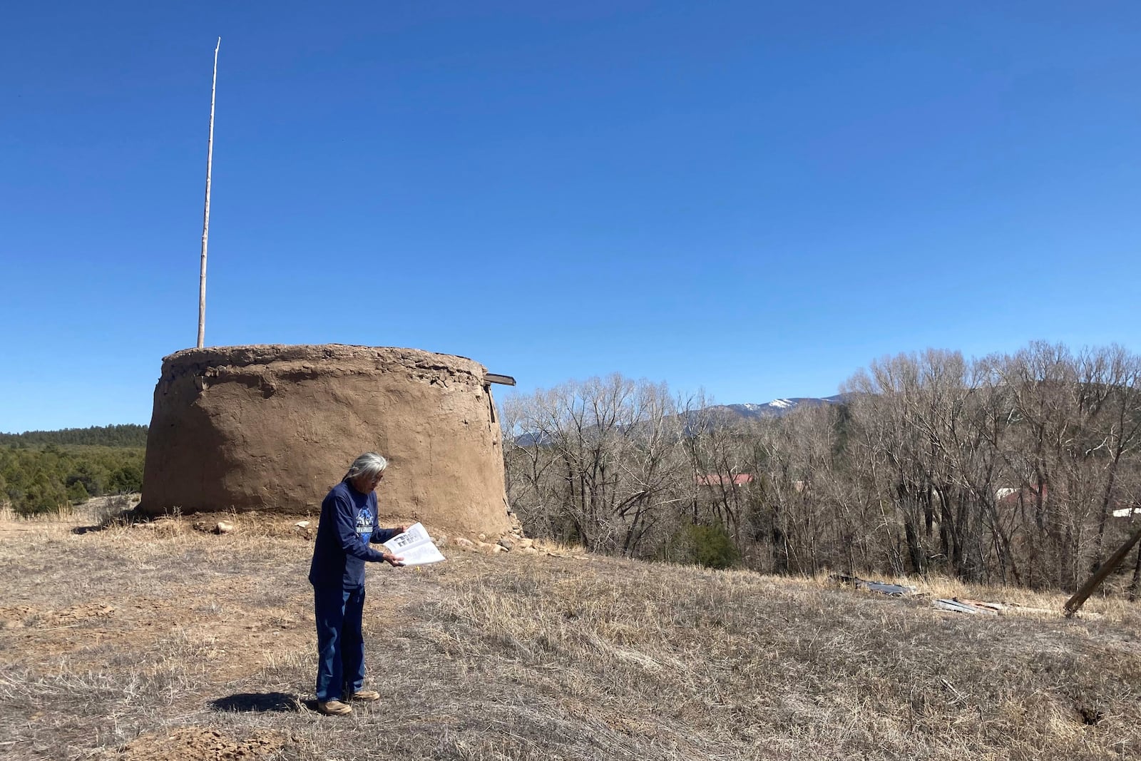 In this photo provided by researchers, Clifford Tsosie stands in front of the Round House in Picuris Pueblo, N.M., in April 2024. It is one of the Picuris' ritual rooms, used by members of the summer and winter society for rituals and meetings. (Thomaz Pinotti via AP)