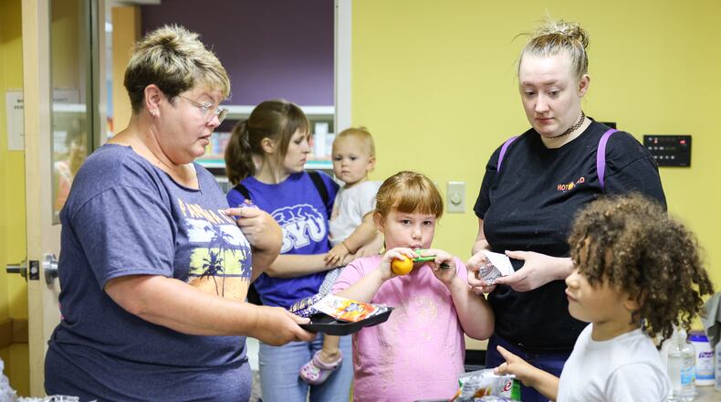 Chris Burge (far left), a child nutrition specialist at Fairborn Middle School, talks to a child during a summer lunch session on Friday, July 25 at Fairborn Library. Kayleigh Jones (center right, in black) attended the lunch with her younger siblings Rilee (center) and Shayden (right). Fairborn City Schools provides free meals to children ages 1 to 18 at 10 different sites around the city each weekday from June 9 to Aug. 1. BRYANT BILLING / STAFF