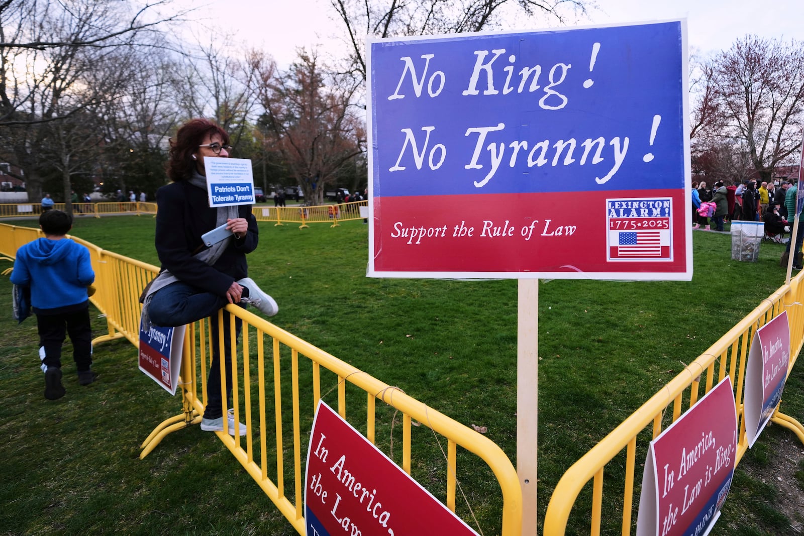 A lone protestor sits in the "Free Speech Zone" during a reenactment celebration of the 250th anniversary of the Battle of Lexington and start of the American Revolution, Saturday, April 19, 2025, in Lexington, Mass. (AP Photo/Charles Krupa)