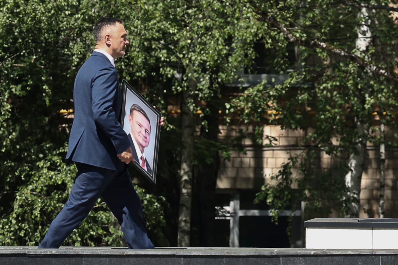 A man carries a portrait of Roman Starovoit, the former transport minister who died in an apparent suicide after his dismissal while people line up to his bid farewell, at the morgue of the Central Clinical Hospital in Moscow, Russia, Thursday, July 10, 2025. (AP Photo)