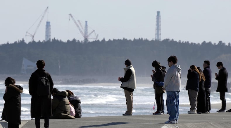 People observe a moment of silence at 2:46 p.m., the moment the earthquake struck with a backdrop of Fukushima Daiichi nuclear power plant in Namie, Fukushima prefecture, northern Japan as the country marked the 15th anniversary of the massive earthquake, tsunami and nuclear disaster. (Kyodo News via AP)