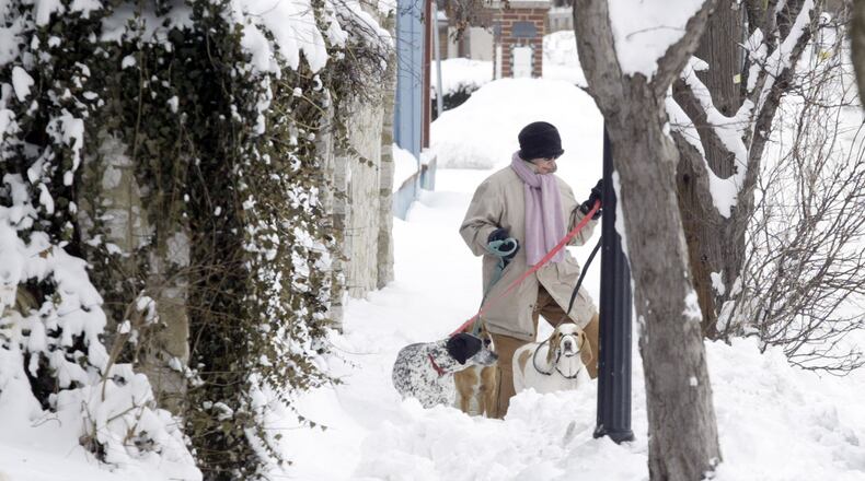 This 2008 photo shows a woman walking around the sidewalk with her three dogs because of almost a foot of snow covers the McPherson Town sidewalks in Dayton. STAFF/FILE
