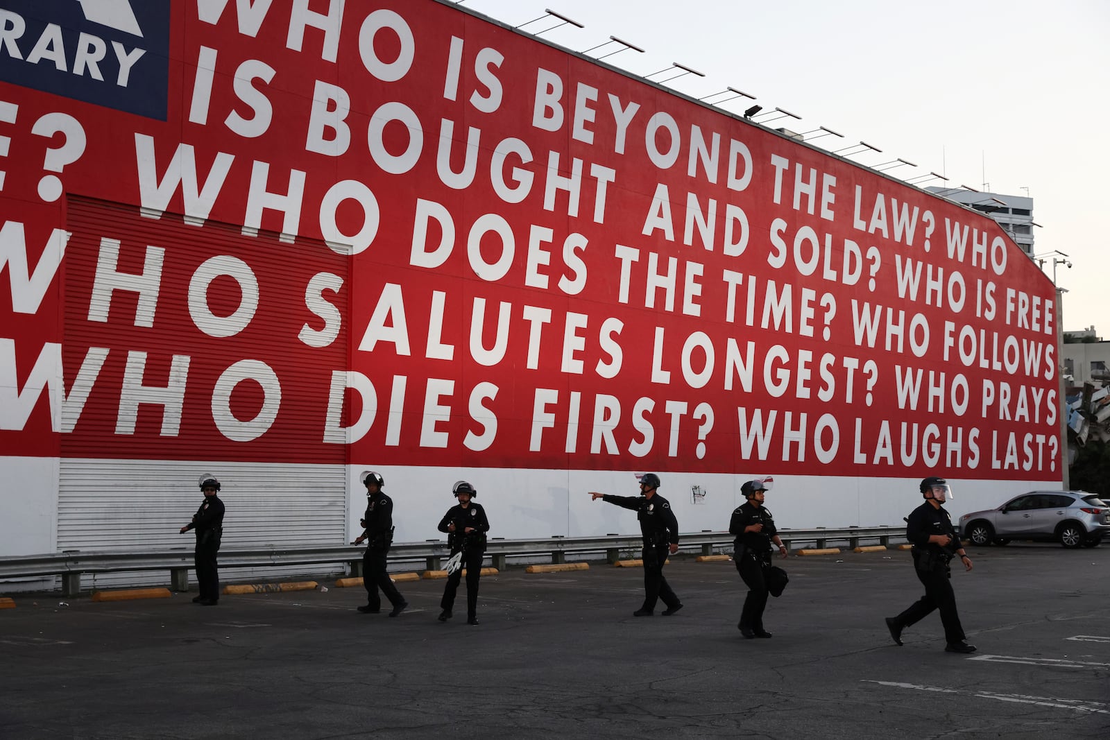 Los Angeles police officers form up beneath a mural by artist Barbara Kruger while protesters rally during a demonstration in response to a series of United States Immigration and Customs Enforcement (ICE) raids throughout the country, in Los Angeles, Calif., Thursday, June 12, 2025. (Gabrielle Lurie/San Francisco Chronicle via AP)