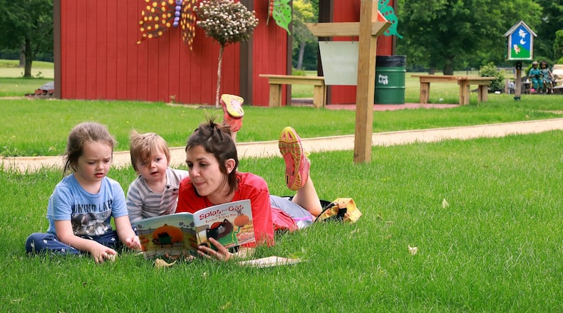 Trena Courey lies in the grass reading to her children, Callie, and Ezra at the Springfield Kiwanis Children’s Garden at Snyder Park Wednesday. BILL LACKEY/STAFF