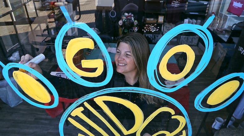 Tracey Tackett decorates the front window of Sip & Dipity Paint Bar to show her support of the Springfield Wildcats Football team on Friday. BILL LACKEY/STAFF