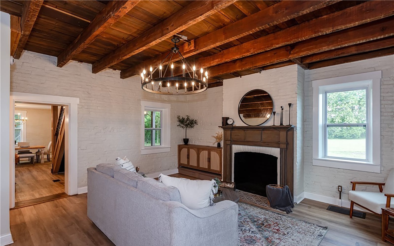 The living room has a wood beamed ceiling with a decorative chandelier, a fireplace, exposed brick walls and LVT flooring. CONTRIBUTED