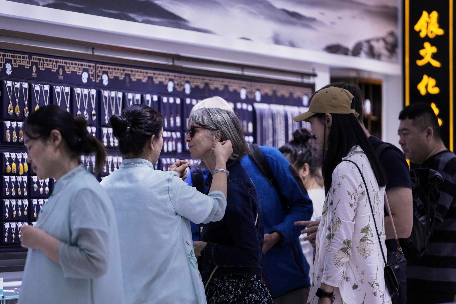 A tourist tries out an earring as they visit a fashion jewelry store at Qianmen pedestrian shopping street in Beijing, Sunday, April 27, 2025. (AP Photo/Andy Wong)